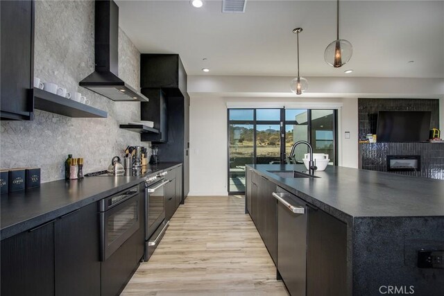 kitchen featuring a spacious island, pendant lighting, wall chimney exhaust hood, stainless steel appliances, and sink