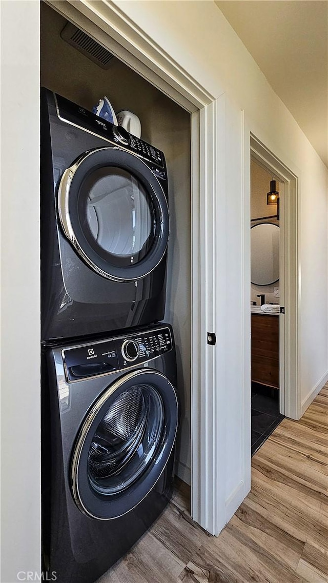 laundry room featuring wood-type flooring and stacked washer and clothes dryer