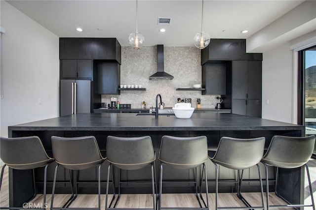 kitchen with high quality fridge, a kitchen breakfast bar, sink, and wall chimney range hood