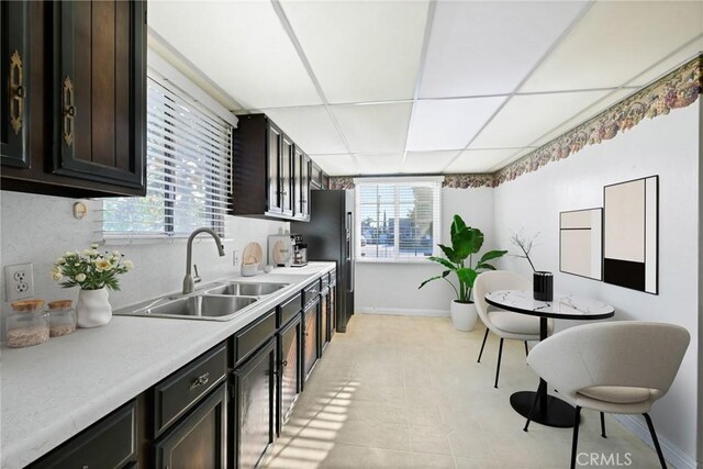 kitchen featuring stainless steel fridge, dark brown cabinetry, a drop ceiling, and sink