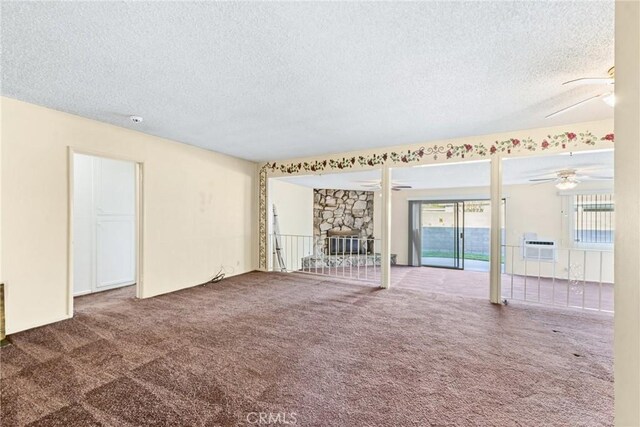 empty room featuring carpet flooring, a textured ceiling, and a stone fireplace