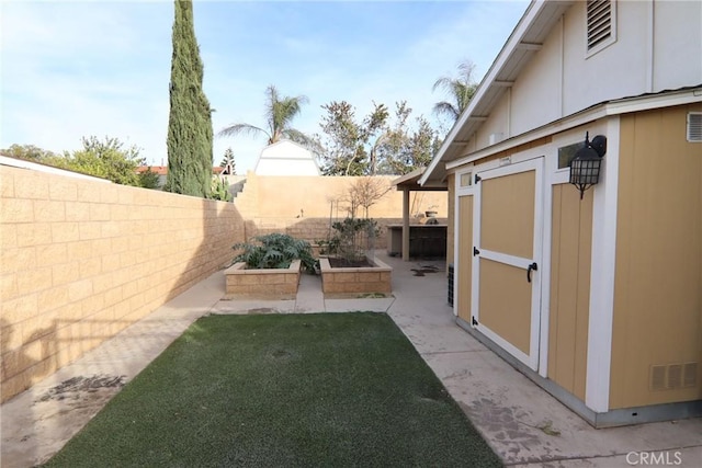 view of yard with an outbuilding, a fenced backyard, visible vents, a vegetable garden, and a storage unit