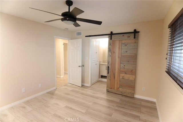 unfurnished bedroom with visible vents, light wood-style flooring, ensuite bathroom, a barn door, and baseboards