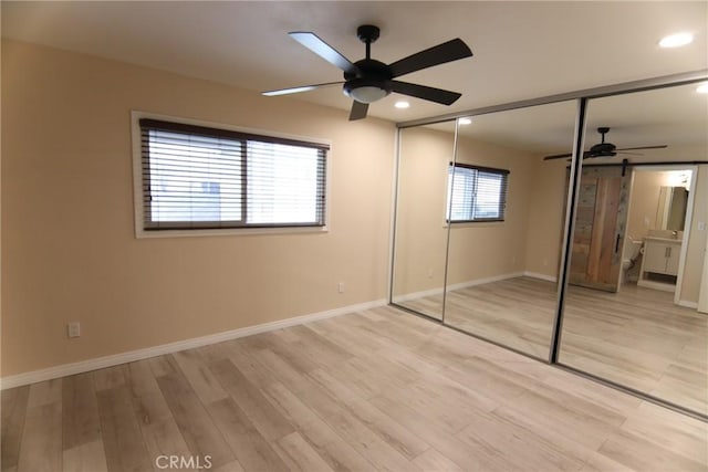 unfurnished bedroom featuring light wood-type flooring, a barn door, baseboards, and recessed lighting