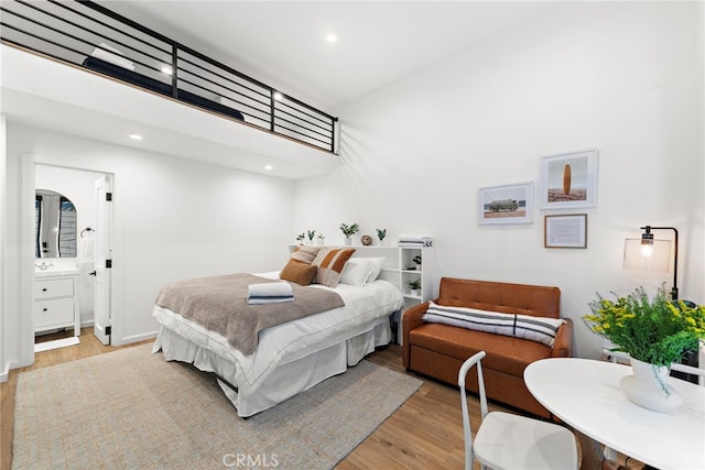 bedroom featuring ensuite bathroom, light hardwood / wood-style flooring, and a towering ceiling