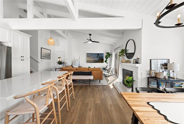 dining area with a brick fireplace, beamed ceiling, high vaulted ceiling, hardwood / wood-style floors, and ceiling fan with notable chandelier