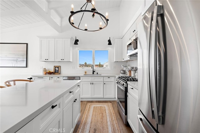 kitchen featuring lofted ceiling with beams, white cabinets, stainless steel appliances, and an inviting chandelier