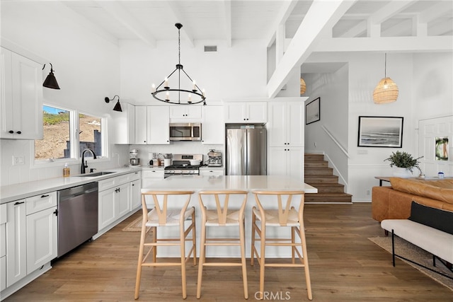 kitchen featuring beam ceiling, white cabinetry, a center island, pendant lighting, and appliances with stainless steel finishes