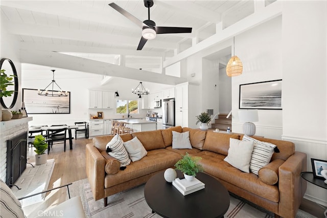 living room with wooden ceiling, vaulted ceiling with beams, a fireplace, ceiling fan with notable chandelier, and light wood-type flooring