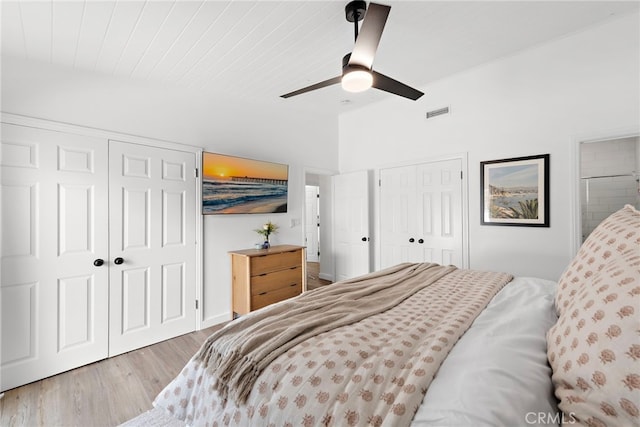 bedroom featuring two closets, vaulted ceiling, ceiling fan, light wood-type flooring, and wood ceiling