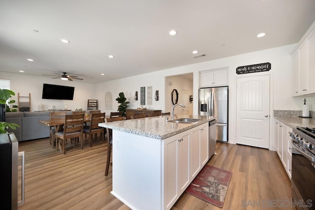 kitchen with sink, white cabinetry, a kitchen island with sink, and light stone countertops