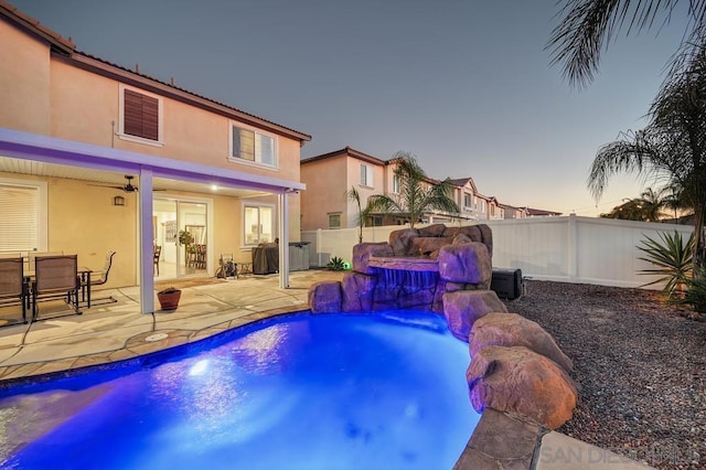 pool at dusk featuring ceiling fan, pool water feature, and a patio area