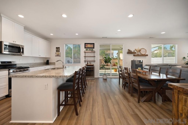 kitchen with a kitchen breakfast bar, a kitchen island with sink, appliances with stainless steel finishes, white cabinets, and sink