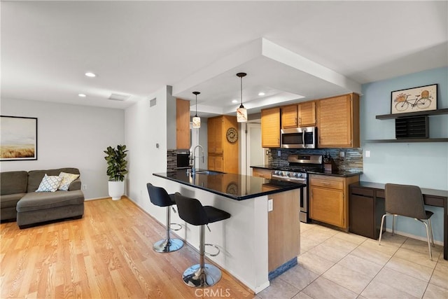 kitchen featuring kitchen peninsula, appliances with stainless steel finishes, a kitchen bar, sink, and hanging light fixtures