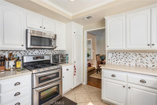 kitchen featuring light tile patterned floors, white cabinetry, stainless steel appliances, backsplash, and crown molding