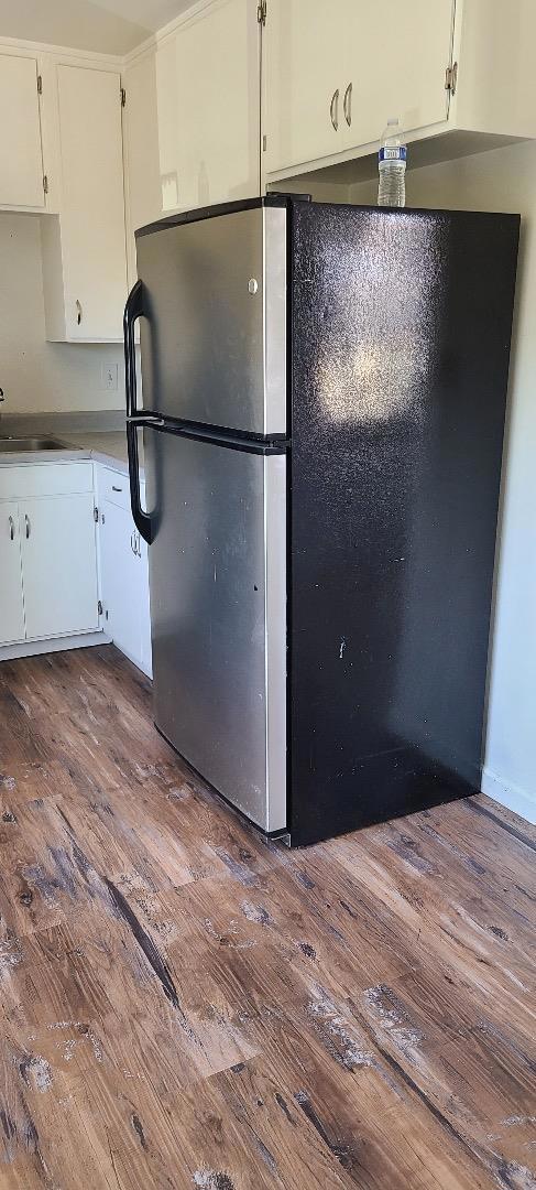 kitchen with hardwood / wood-style flooring, stainless steel refrigerator, white cabinetry, and sink