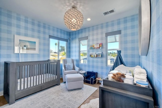 bedroom with a crib, hardwood / wood-style flooring, multiple windows, and a notable chandelier