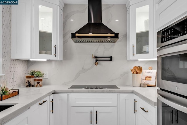 kitchen featuring light stone counters, island range hood, tasteful backsplash, black electric stovetop, and white cabinets