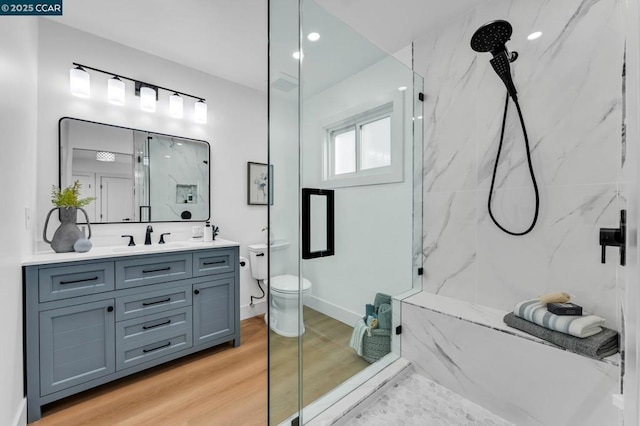 bathroom with toilet, a tile shower, wood-type flooring, and vanity