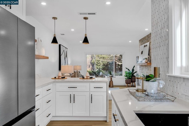 kitchen featuring light stone countertops, light hardwood / wood-style flooring, hanging light fixtures, stainless steel refrigerator, and white cabinets