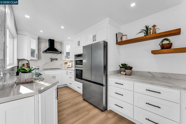 kitchen featuring light stone countertops, stainless steel appliances, wall chimney range hood, light hardwood / wood-style floors, and white cabinetry