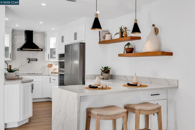 kitchen with light stone countertops, ventilation hood, stainless steel fridge, a kitchen bar, and white cabinetry