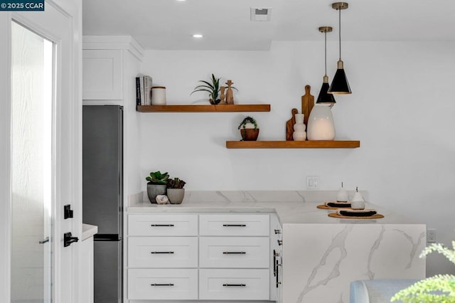 kitchen featuring white cabinets, pendant lighting, light stone countertops, and stainless steel refrigerator