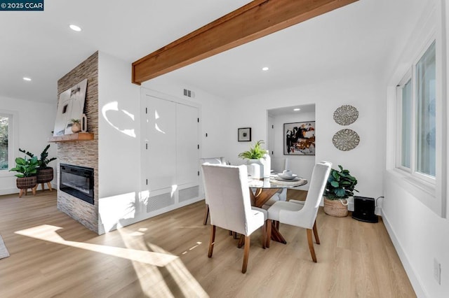 dining room featuring a fireplace, light wood-type flooring, and beamed ceiling