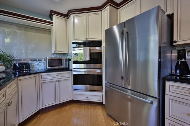 kitchen featuring appliances with stainless steel finishes, dark stone countertops, light hardwood / wood-style flooring, and tasteful backsplash