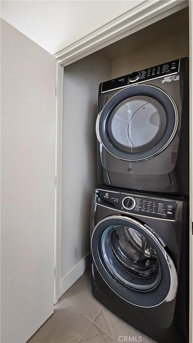 laundry room featuring stacked washer / drying machine and light tile patterned floors