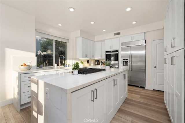 kitchen featuring sink, light hardwood / wood-style flooring, appliances with stainless steel finishes, white cabinets, and a kitchen island