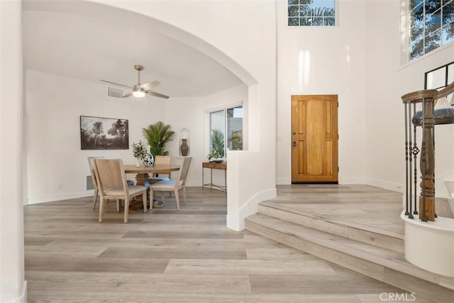 entryway with ceiling fan, a towering ceiling, and light wood-type flooring