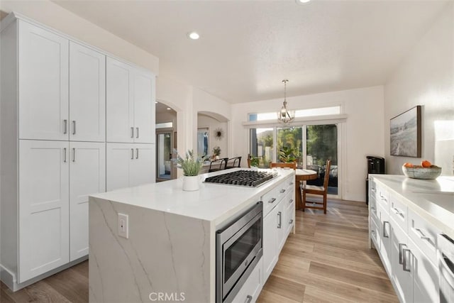 kitchen with stainless steel appliances, a kitchen island, hanging light fixtures, and white cabinets