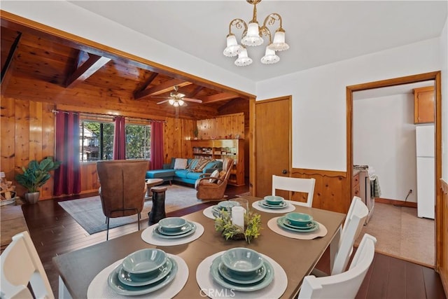 dining space featuring vaulted ceiling with beams, ceiling fan with notable chandelier, dark wood-type flooring, and wood walls