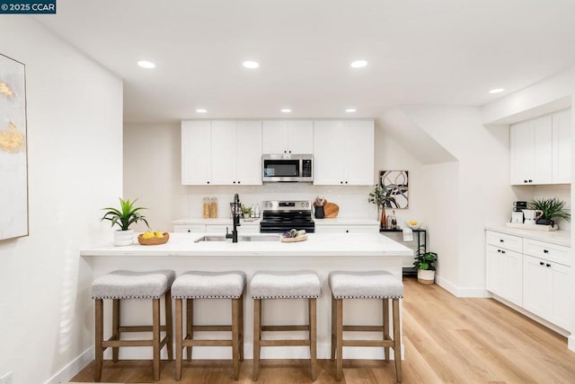 kitchen featuring kitchen peninsula, appliances with stainless steel finishes, a kitchen breakfast bar, and white cabinetry