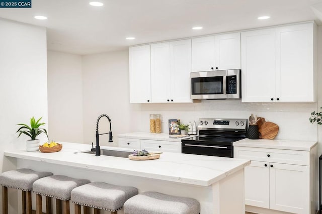 kitchen with a breakfast bar, sink, light stone countertops, appliances with stainless steel finishes, and white cabinets