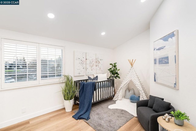 bedroom featuring hardwood / wood-style floors, a nursery area, and lofted ceiling