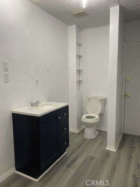 bathroom featuring vanity, wood-type flooring, a textured ceiling, and toilet