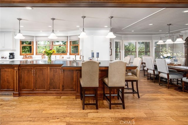 kitchen featuring white cabinetry, crown molding, decorative light fixtures, and light wood-type flooring