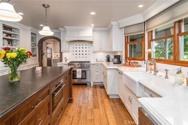 kitchen featuring light stone countertops, high end stove, pendant lighting, light hardwood / wood-style floors, and white cabinetry