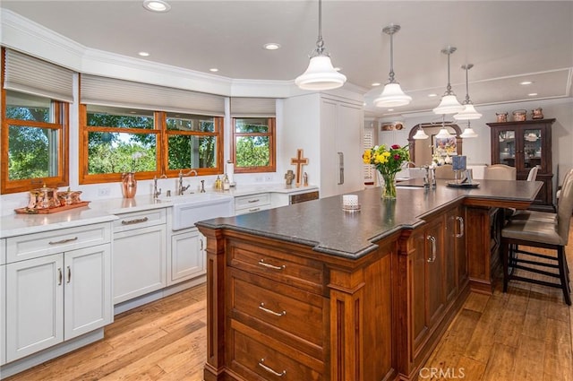 kitchen featuring light wood-type flooring, sink, pendant lighting, a center island, and white cabinetry