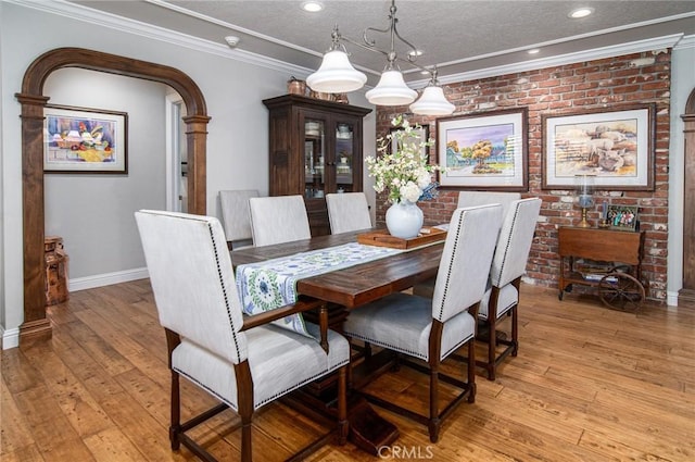 dining space featuring light wood-type flooring, crown molding, and brick wall