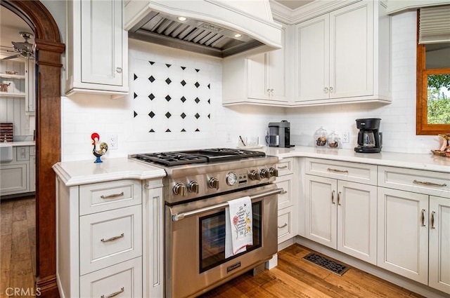 kitchen with custom exhaust hood, high end range, backsplash, white cabinets, and hardwood / wood-style flooring