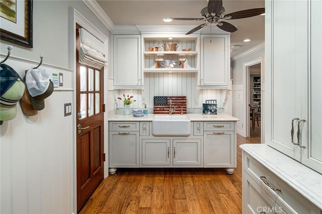 bar featuring ornamental molding, ceiling fan, sink, wood-type flooring, and white cabinets