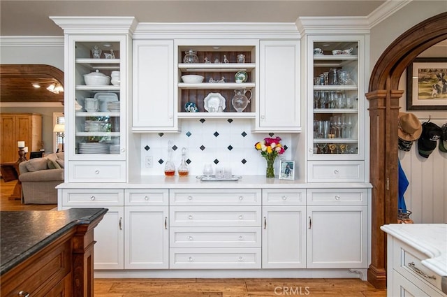 bar with dark stone countertops, decorative backsplash, white cabinets, and light wood-type flooring