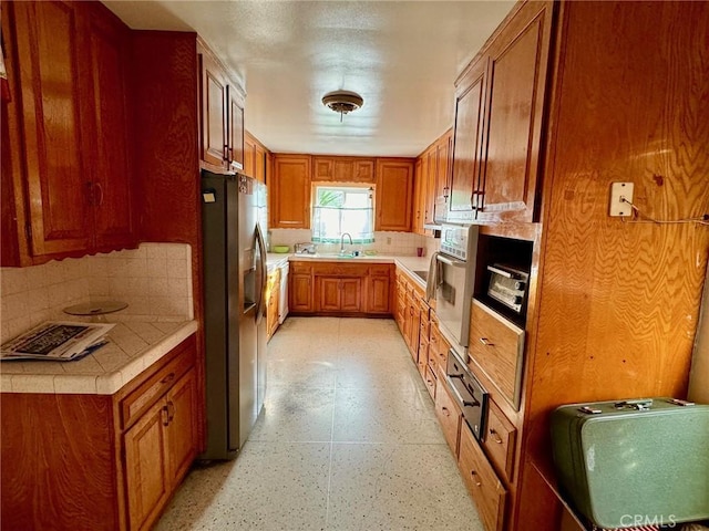 kitchen featuring decorative backsplash, oven, stainless steel fridge with ice dispenser, and sink