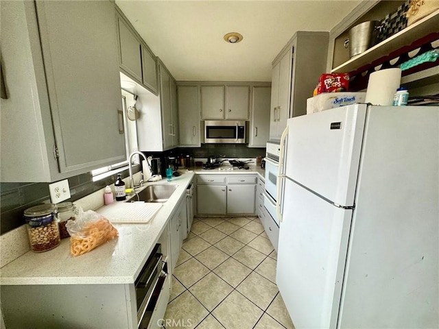 kitchen with gray cabinetry, sink, light tile patterned flooring, and white appliances