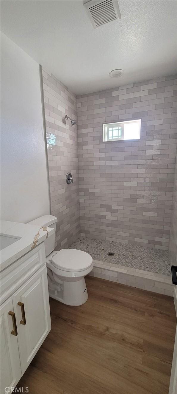 bathroom featuring toilet, hardwood / wood-style flooring, a tile shower, and vanity