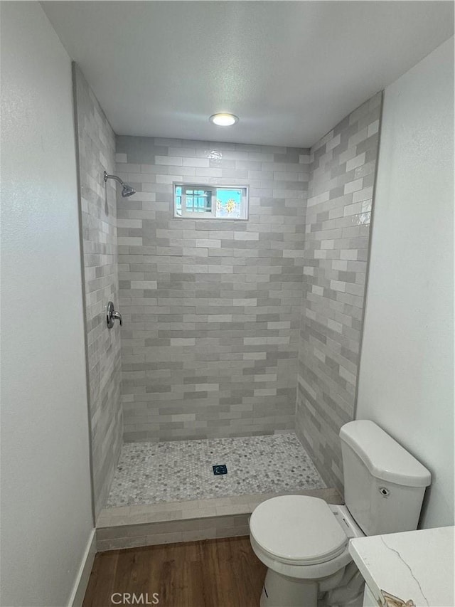 bathroom with a tile shower, vanity, toilet, and hardwood / wood-style floors