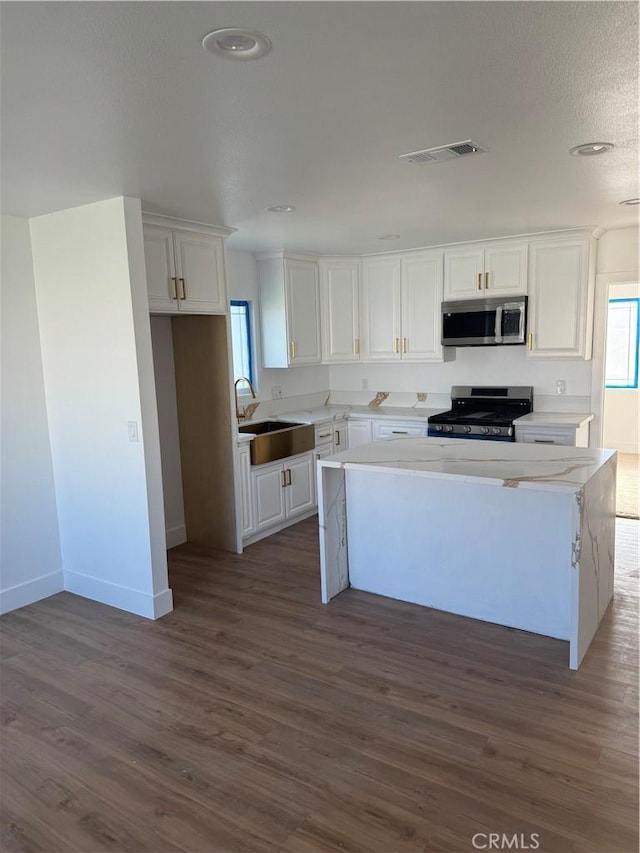 kitchen with stainless steel appliances, a wealth of natural light, a kitchen island, sink, and white cabinetry